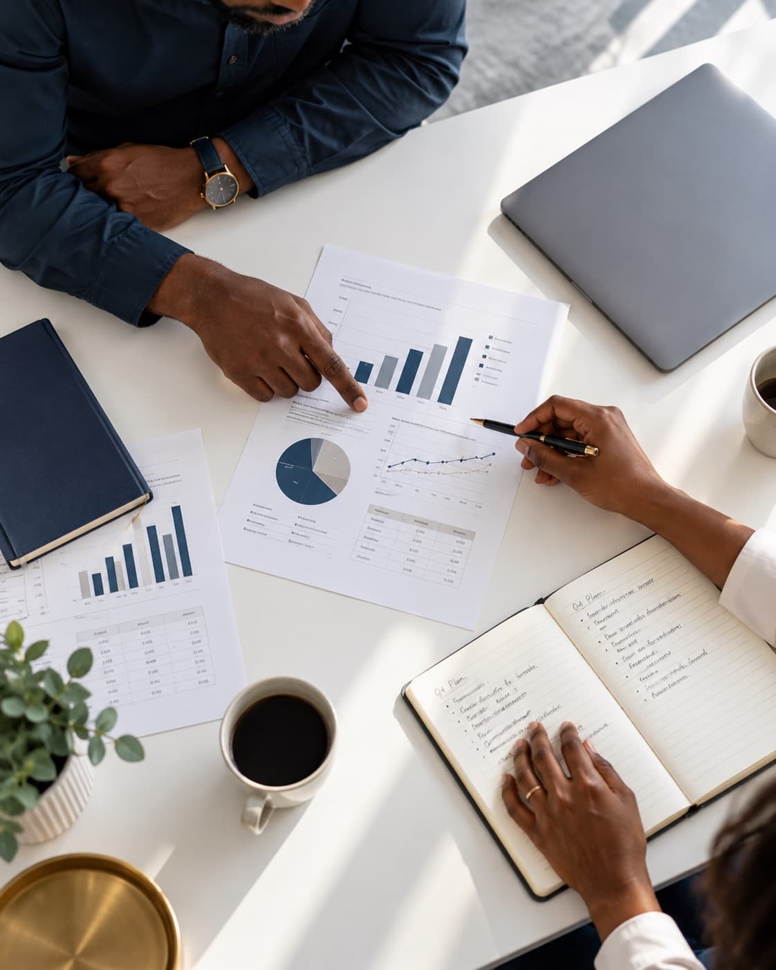 Two people at a white table review printed forecasts and take notes together.